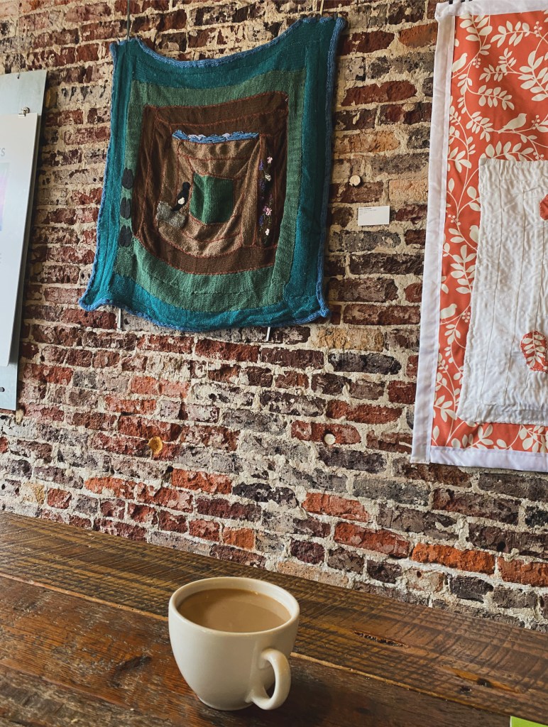 a coffee cup on a table with quilts hanging on a wall